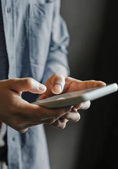 Nahaufnahme von Händen in einem hellblauen Hemd, die ein Smartphone bedienen.